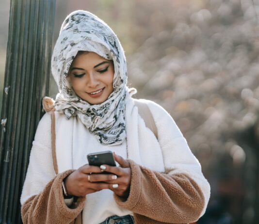 Maintaining Your Body Temperature in Extremely Cold Weather cheerful young ethnic female in headscarf and coat browsing smartphone