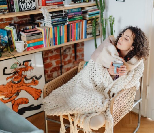 Sore Throat Remedies That Work woman feeling cold wrapped in a shawl and drinking tea