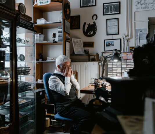 Is It Dangerous for to Rub Your Eyes Too Much? a man in white long sleeves and black vest sitting on a chair while rubbing his eyes