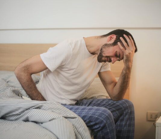 Flu Lingers in the US, Exhibiting Mixed Patterns of Decline and Escalation young man in sleepwear suffering from headache in morning