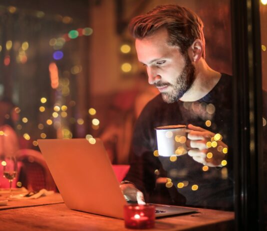 Caffeine May Help Prevent Weight Gain and Reduce Risk of Joint Diseases man holding mug in front of laptop