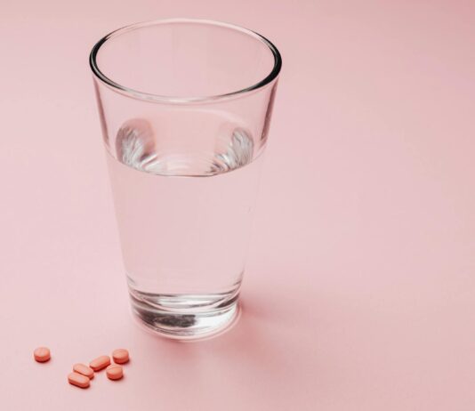 This Cholesterol Drug Could Remove PFAS from Blood photo of glass of water beside capsules